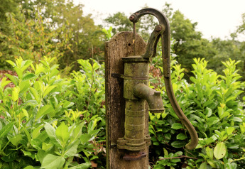 Alte Wasserpumpe vor grünen Büschen am Lodge „Le Chession“ in Belgien, draußen aufgenommen.