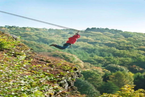 Een persoon met een rode trui suist aan de zipline bij lodge Le Chession, omgeven door Belgisch bos.