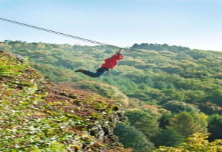 Een persoon met een rode trui suist aan de zipline bij lodge Le Chession, omgeven door Belgisch bos.