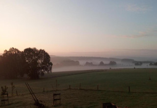 Ochtendmist over een groen veld bij lodge Le Chession in België met bomen en nevel in de verte.