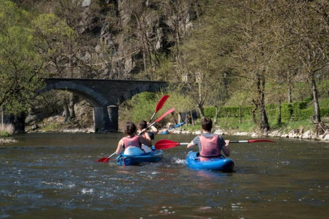 Mensen kajakken op een rivier bij Le Chession in België met een stenen brug en veel groen op de achtergrond.