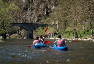 Mensen kajakken op een rivier bij Le Chession in België met een stenen brug en veel groen op de achtergrond.
