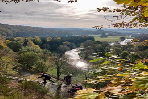 Uitzicht vanaf lodge Le Chession in België, met een rivierdal en mensen die via een ladder klimmen.