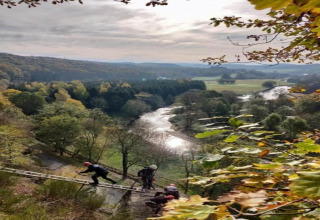 Uitzicht vanaf lodge Le Chession in België, met een rivierdal en mensen die via een ladder klimmen.