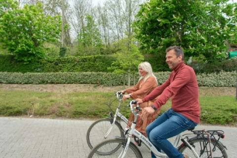 Dos adultos montan en bicicleta juntos cerca de Resort Beachside 5, Bélgica, rodeados de naturaleza.