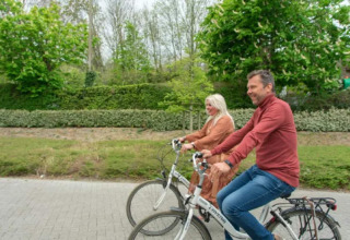 Dos adultos montan en bicicleta juntos cerca de Resort Beachside 5, Bélgica, rodeados de naturaleza.