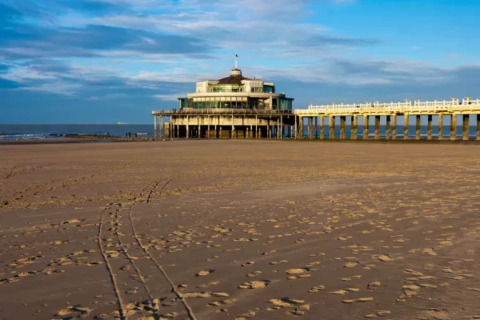 Playa con huellas y un muelle con edificio circular, foto tomada en el Resort Beachside 5 en Bélgica.