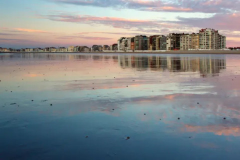 Vista de la playa con edificios altos reflejados al atardecer cerca del Resort Beachside 5 en Bélgica.
