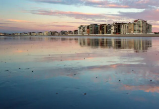 Vista de la playa con edificios altos reflejados al atardecer cerca del Resort Beachside 5 en Bélgica.
