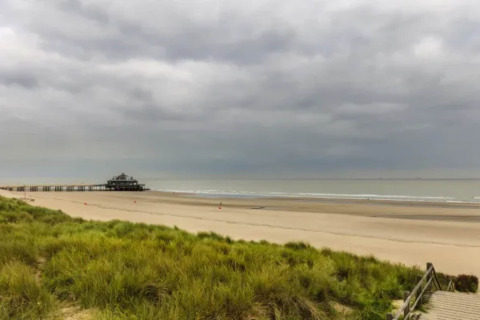 Vista de playa tranquila con dunas, muelle y cielo nublado en Resort Beachside 5, Bélgica.