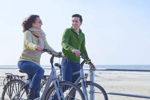 Dos personas en bicicleta en la playa junto al Resort «Beachside 5» en Bélgica, disfrutando el día.