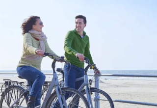 Dos personas en bicicleta en la playa junto al Resort «Beachside 5» en Bélgica, disfrutando el día.