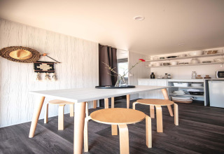 Interior luminoso de tienda safari en Resort Beachside 5, Bélgica, con mesa y taburetes de madera claros.