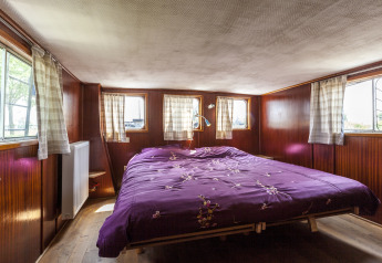 Camera da letto con pareti di legno e copriletto viola sulla casa galleggiante ‘St Antoine Isera’ in Belgio.