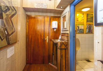Area bagno sulla casa galleggiante St Antoine Isera in Belgio con porta in legno, lavandino e orinatoio.