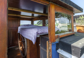 Interno della houseboat 'St Antoine Isera' in Belgio con pannelli di legno, letto e timone grande.