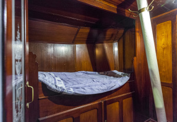 Letto in cabina di legno con coperta blu sulla houseboat St Antoine Isera fotografata in Belgio.