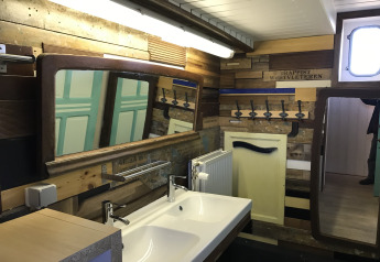 Bagno sulla casa galleggiante St Antoine Isera in Belgio con doppi specchi, lavabo e pareti in legno.