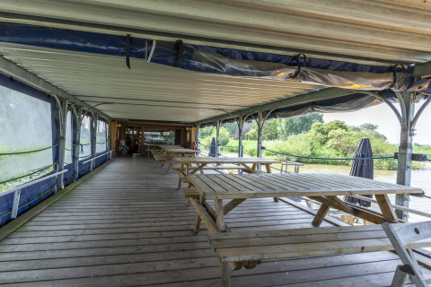 Udendørs træterrasse med picnicborde på husbåden St Antoine Isera i Belgien, rolig udsigt til natur.