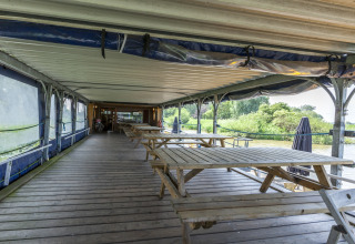 Udendørs træterrasse med picnicborde på husbåden St Antoine Isera i Belgien, rolig udsigt til natur.