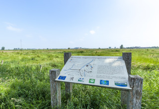 Informationsskilt ved fuglereservatet IJzervallei i Belgien med udsigt over grønne enge og det åbne landskab.