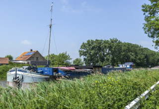 Husbåd ved navn St Antoine Isera fortøjet ved en grøn kanal i Belgien med hus og træer i baggrunden.