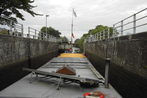 Foto von einem Hausboot in einer engen Schleuse mit hohen Betonwänden und Geländern an den Seiten.