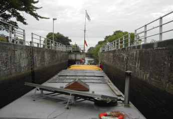 Foto scattata da una casa galleggiante situata in una stretta chiusa con alte pareti di cemento e ringhiere.