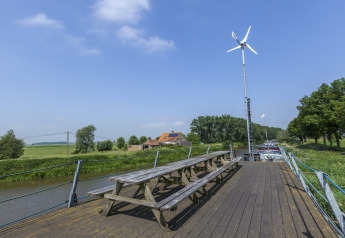 Panche di legno sulla casa galleggiante St Antoine Isera in Belgio con turbina eolica e panorama rurale.