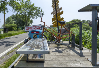 Bicicletta e segnali sulla casa galleggiante vicino alla strada in Belgio, con campi verdi intorno.