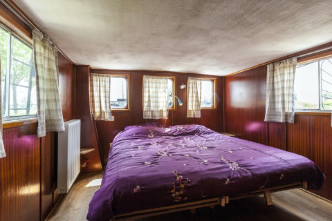 Schlafzimmer mit lila Bett und Holzverkleidung auf dem Hausboot St Antoine in Belgien mit Fenstern.