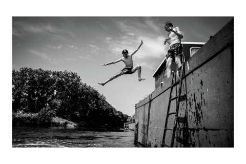 Zwei Jungen springen von dem Hausboot St Antoine in Belgien zum Wasser, fröhlicher Sommertag.