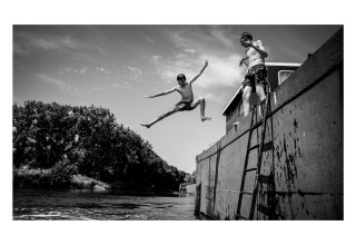 Zwei Jungen springen von dem Hausboot St Antoine in Belgien zum Wasser, fröhlicher Sommertag.