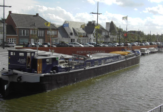 Hausboot St Antoine liegt am Kanal in Belgien, mit Stadtgebäuden und geparkten Autos im Hintergrund.