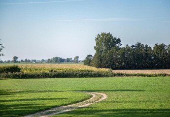 Landskabsfoto taget fra husbåden 'St Antoine' i Belgien, med grøn mark og træer i baggrunden.