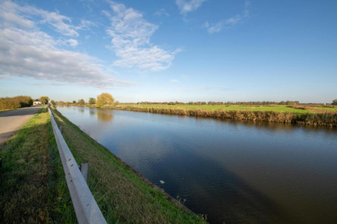 Blick von dem Hausboot 'St Antoine' in Belgien, mit einem ruhigen Kanal, Wiesen und blauem Himmel.