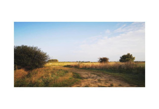 Ländliche Landschaft mit Feldweg bei Hausboot 'St Antoine' in Belgien, unter blauem Himmel und Wolken.