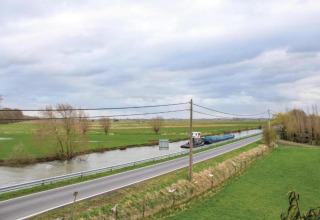 Blick vom Hausboot „St Antoine“ in Belgien auf grüne Felder, eine Straße und einen Kanal mit Boot.