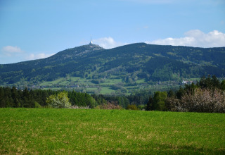 Vista dal chalet Marcela in Repubblica Ceca con prati verdi, foreste e una montagna sormontata da una torre.