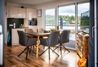 Interno di una moderna houseboat con cucina, zona pranzo e grandi finestre affacciate sul lago Bärwalder See.