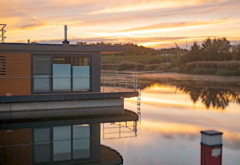 Das Hausboot Houseboat am Bärwalder See liegt auf dem Wasser bei Sonnenuntergang mit schönen Spiegelungen.