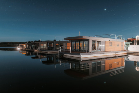 Moderne case galleggianti con grandi vetrate su un lago calmo sotto un cielo stellato al Bärwalder See.