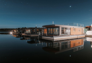 Moderne husbåd med store vinduer flyder på en stille sø under en stjerneklar nat ved Bärwalder See.