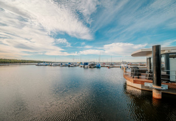 Blick auf den Bärwalder See mit Hausboot am Steg und mehreren Booten unter blauem Himmel.