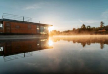 Sonnenaufgang bei Houseboat am Bärwalder See mit Spiegelung auf Wasser und sanftem Nebel.