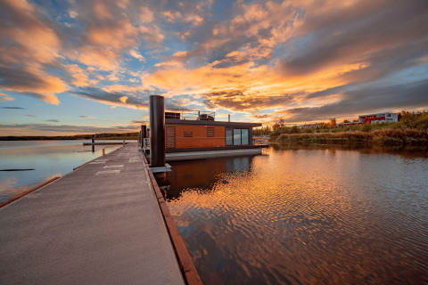 Solnedgang ved Houseboat am Bärwalder See med et moderne husbåd på det rolige vand og en smuk himmel.
