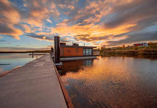 Sunset view of Houseboat am Bärwalder See, featuring a modern houseboat on calm water and vibrant sky.
