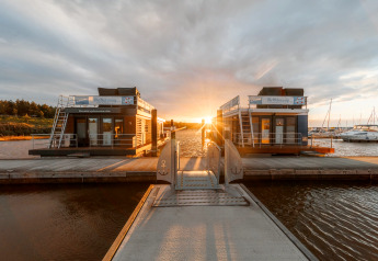 Sonnenuntergang hinter zwei Hausbooten am Bärwalder See, gesehen von einem Steg, umgeben von Wasser.