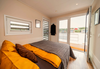Modernes Schlafzimmer im Houseboat am Bärwalder See mit gelber Bettwäsche und Ausblick auf den See.