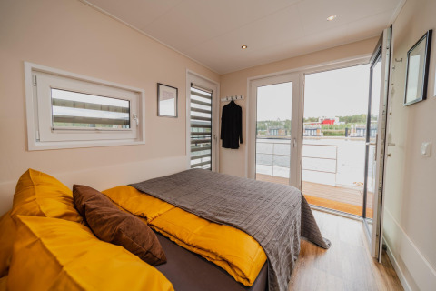 Camera moderna sulla Houseboat am Bärwalder See con biancheria da letto gialla e vista lago dalla terrazza.